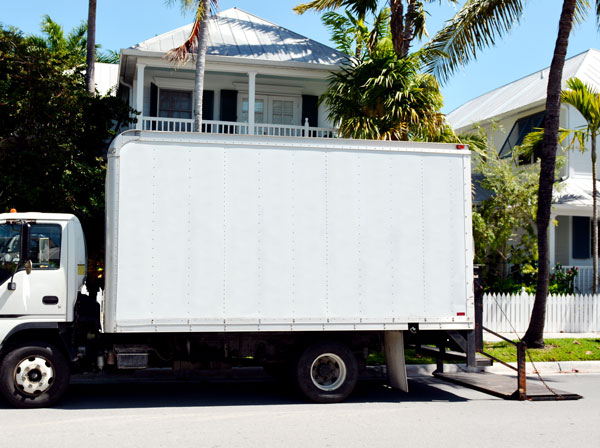 A small white delivery, or moving truck, on a residential street with lift gate lowered onto the street.